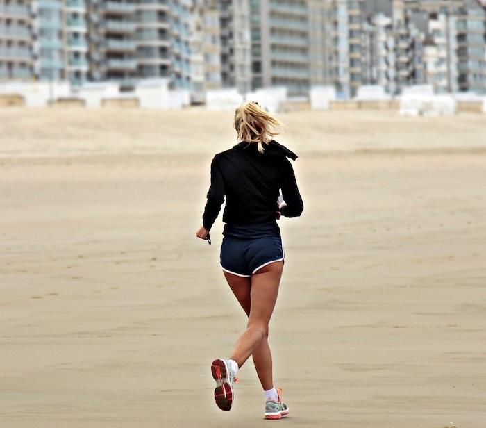 en blond kvinna i shorts och sportkläder som springer på stranden