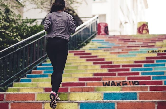 kvinna i svarta byxor klättrar i mångfärgade trappor i staden