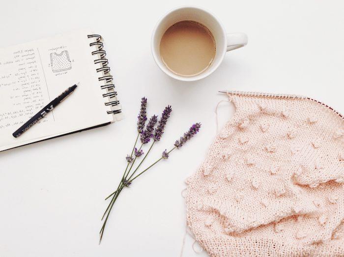 ett vitt bord med några lavendelblommor, en kaffekopp och en anteckningsbok