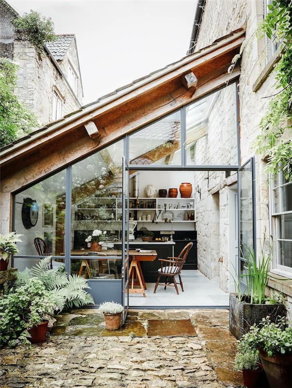 شرفة بجوار المنزل محمية بسقف زجاجي ومحاطة بالنباتات الخضراء