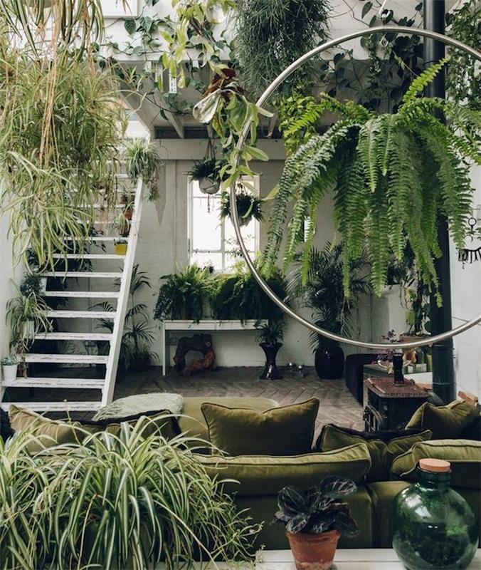 dekorácia v džungli v zarastenej obývačke, olivovo zelená sedačka, biele schodisko, niekoľko závesných rastlín