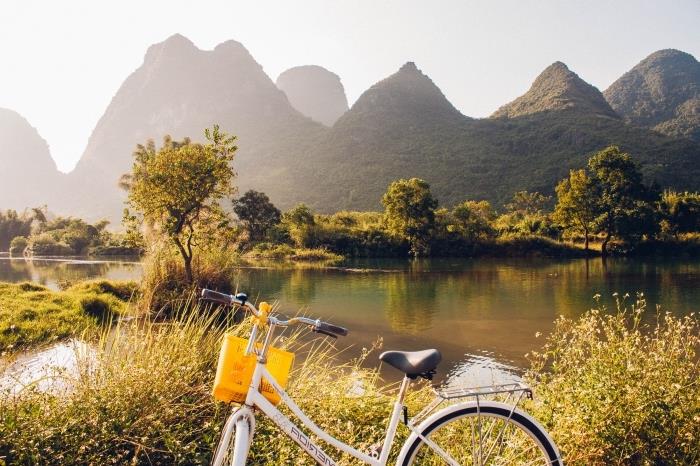 príklad peknej tapety s bielym a čiernym bicyklom pred veľkým jazerom a zelenými horskými kopcami osvetlenými slnečnými lúčmi