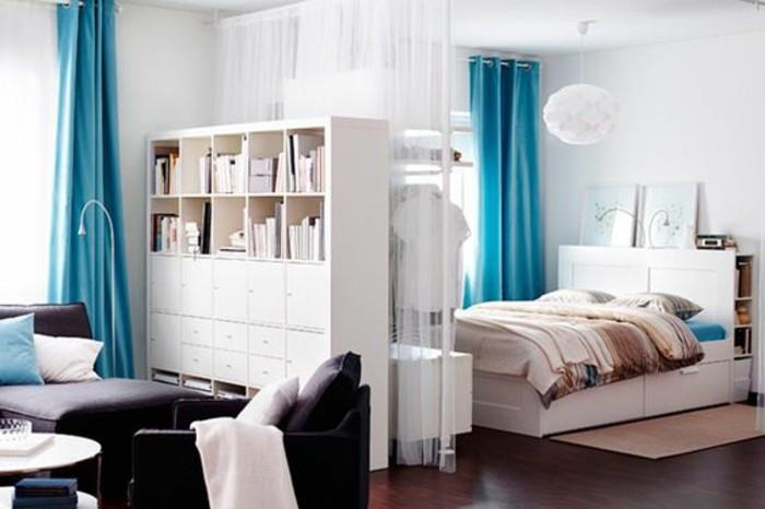 أفكار للشقق الصغيرة ، تعتيم أزرق وستائر بيضاء شفافة ، داخل شقة استوديو ، مع سرير وأريكة ، وخزانة بيضاء وأرضية خشبية بنية داكنة