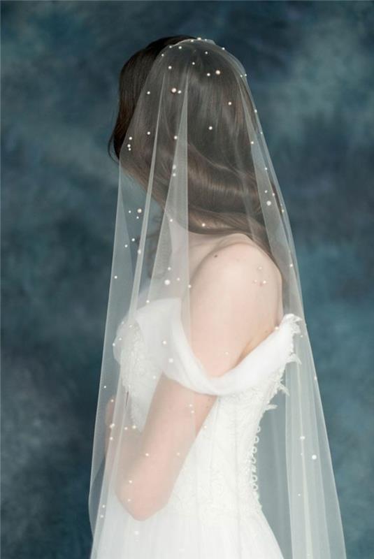 rozprávkový svadobný závoj ozdobený perlami a svadobným účesom s rozpustenými vlasmi, šatami na plece