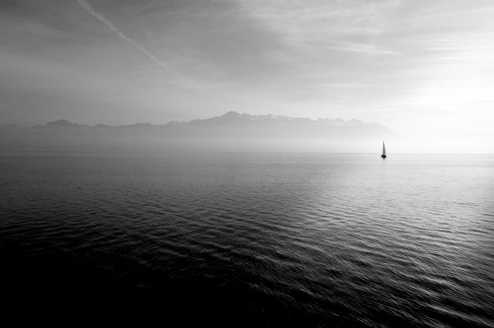 avlägsen silhuett av en segelbåt som simmar i det lugna vattnet i havet, svartvitt fotografi av havslandskap