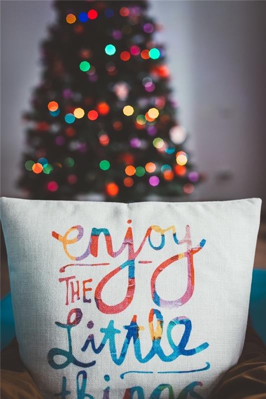 útulná fotografická vianočná dekorácia s vankúšom s inšpiratívnymi viacfarebnými písmenami a veľkým vianočným stromčekom ozdobeným svetlou girlandou