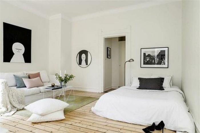 أعمال فنية مربعة ومستديرة باللونين الأبيض والأسود ، داخل غرفة بسيطة ، وكيفية تزيين شقة استوديو ، وأرضية خشبية شاحبة ، وأريكة وسرير باللون الأبيض