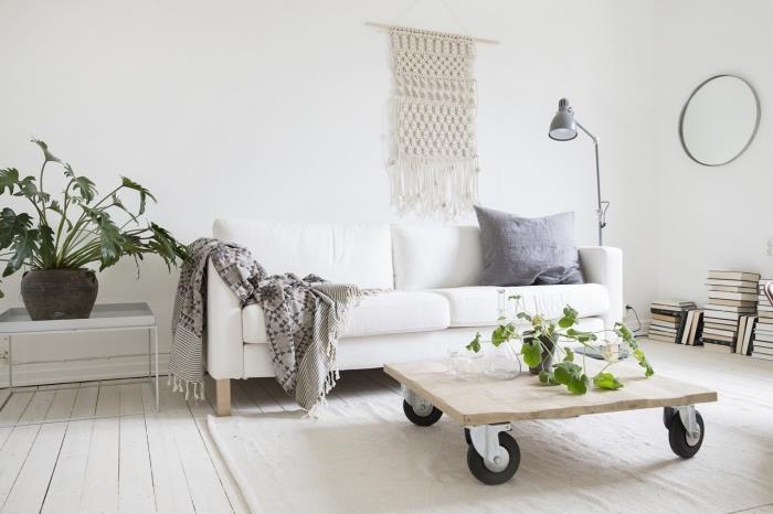 طاولة خشبية على عجلات ، أريكة بيضاء ، أنماط معلقة على الحائط مكرامية مجانية ، بطانية رمادية ، نباتات محفوظ بوعاء