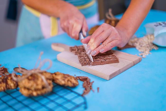 المرأة التي تحمل سكينًا ، قطع الشوكولا ، إلى قطع ، بسكويت رقائق الشوكولا المضغ ، الطاولة الزرقاء ، لوح التقطيع الخشبي
