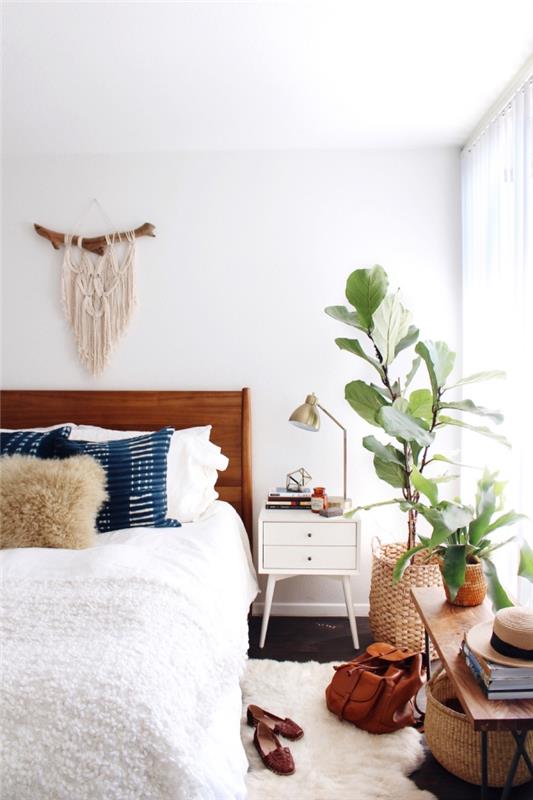 نسيج منسوج معلق على الحائط ، نباتات محفوظ بوعاء ، إطار سرير خشبي ، جدران بيضاء ، وسائد رمي زرقاء